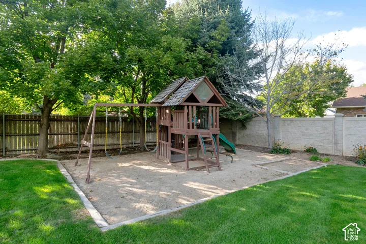 Expansive rear yard featuring a wooden playset with slide, dedicated sand area, and a large grassy lawn