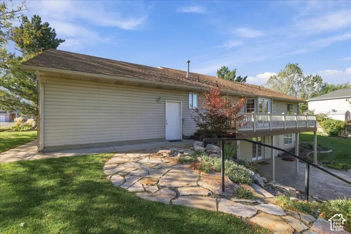 Exterior featuring vinyl siding, an elevated wood deck with white railings, a stone patio, and a covered lower-level concrete terrace