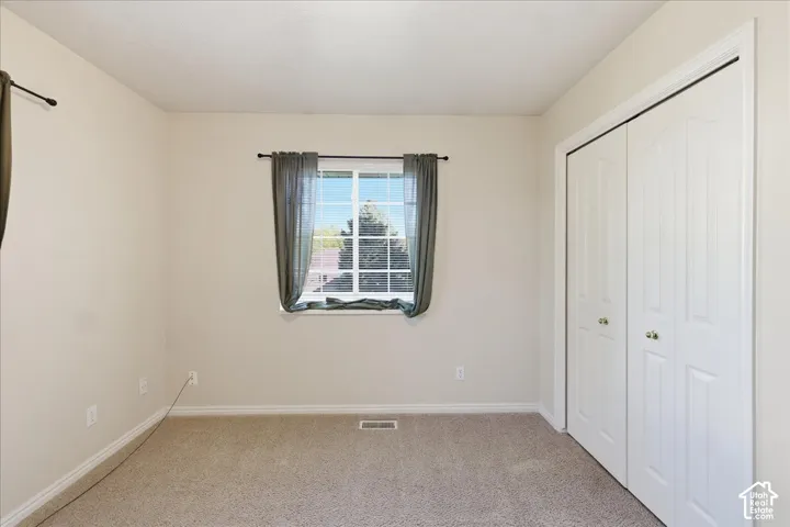 Bedroom #3. Neutral wall finishes, carpeted flooring, window with exterior scenery, and double-panel sliding closet doors