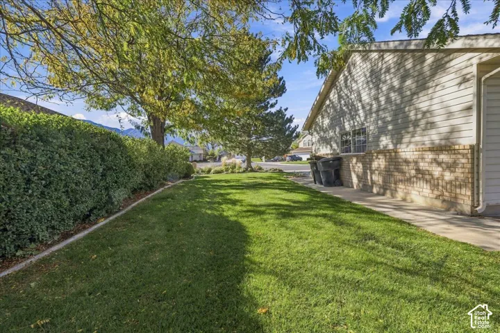 Exterior side yard featuring a concrete walkway, horizontal siding, brick masonry, and mature landscaping