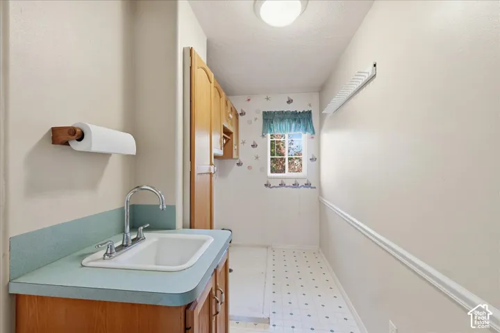 Utility room featuring wood-finish cabinetry, a drop-in sink with a chrome faucet, solid-surface countertop, vinyl flooring, and a wall-mounted drying rack