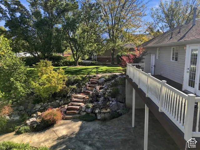 Elevated deck with white balustrades, stone-stepped pathway, integrated rock landscaping, concrete ground-level patio, and horizontal siding