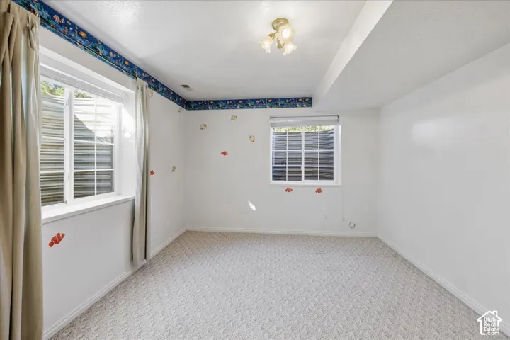Neutral-toned carpeted flooring, dual egress-style windows with integrated wells, and a three-bulb semi-flush mount light fixture