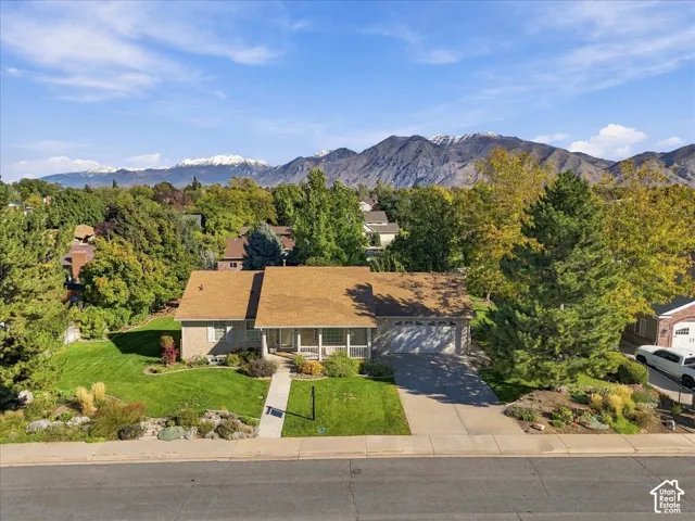 Single-story residence featuring a brick exterior, shingled roof, attached garage, concrete driveway, and mountain backdrop