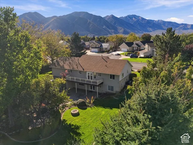 Two-story residence featuring a raised wood deck, paved patio, stone-surround fire pit, mature landscaping, and mountain backdrop