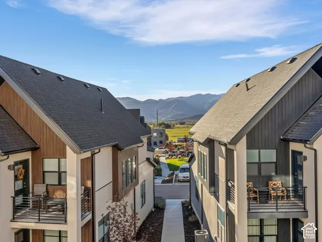 Contemporary townhome exterior featuring an architectural shingle roof, wood-finish siding accents, stucco finish, and a private balcony with metal railings