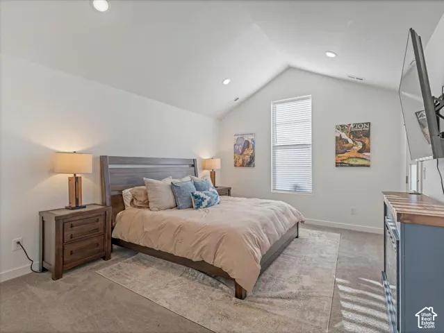 Vaulted ceiling with recessed lighting, large window with blinds, carpeted flooring, and a wood-finish bed frame