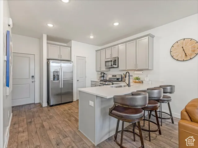 Kitchen featuring wood-finish flooring, stainless steel appliances, light gray cabinetry, and a white countertop with a breakfast bar