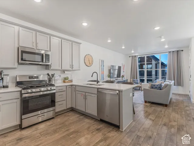 Kitchen with stainless steel appliances, light gray cabinetry, and a central island with a sink