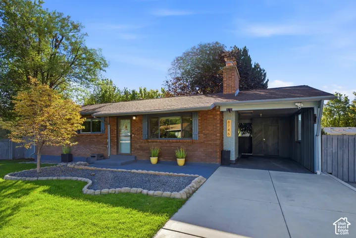 Brick exterior with a covered carport, concrete driveway, and landscaped front yard featuring a gravel bed