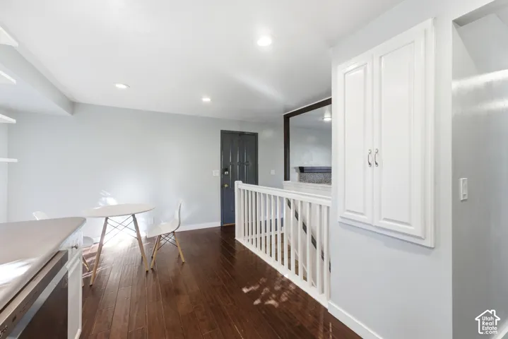 Hardwood-finish flooring, recessed lighting, white wood railing, built-in white cabinetry, and a dark paneled door