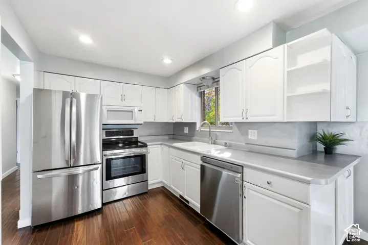 Kitchen featuring wood-finish flooring, white cabinetry, stainless steel appliances, a white sink, and light gray countertops