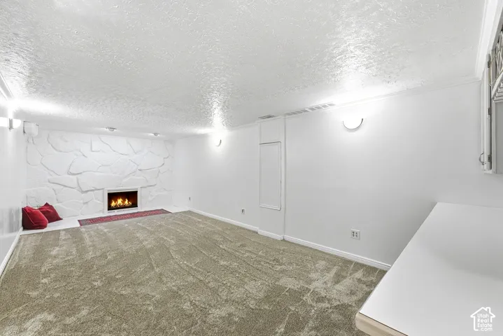 Expansive carpeted area featuring a stone accent wall, a built-in fireplace, and wall-mounted lighting