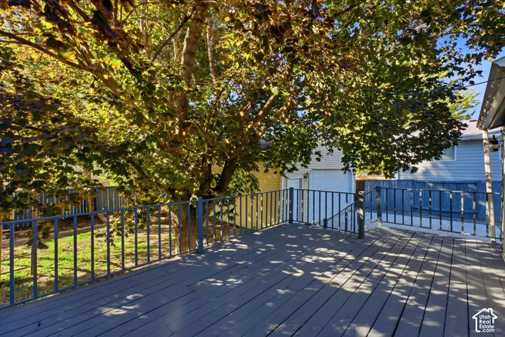 Expansive wooden deck with a durable gray finish, featuring a black metal railing and mature tree canopy