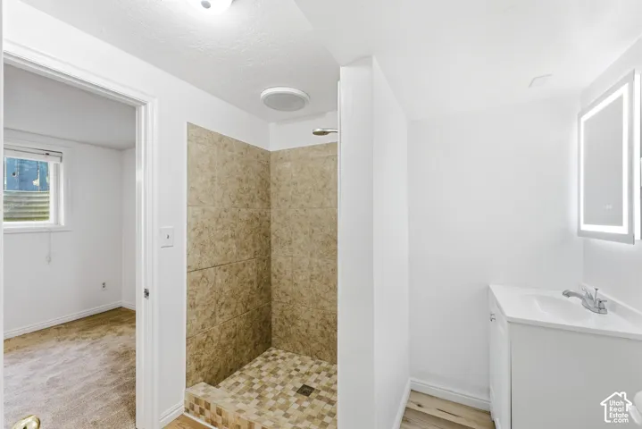 Tiled shower enclosure with mosaic floor, white vanity with integrated sink, and illuminated mirrored cabinet