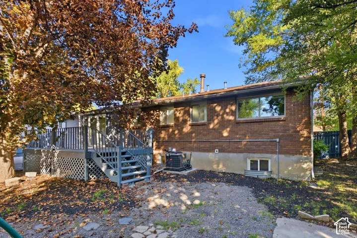 Expansive rear deck with stairs, brick exterior, and mature trees