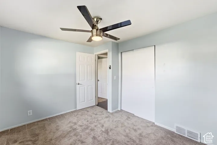 Neutral tone carpeting, light blue wall paint, multi-paneled interior door, and ceiling fan with integrated lighting