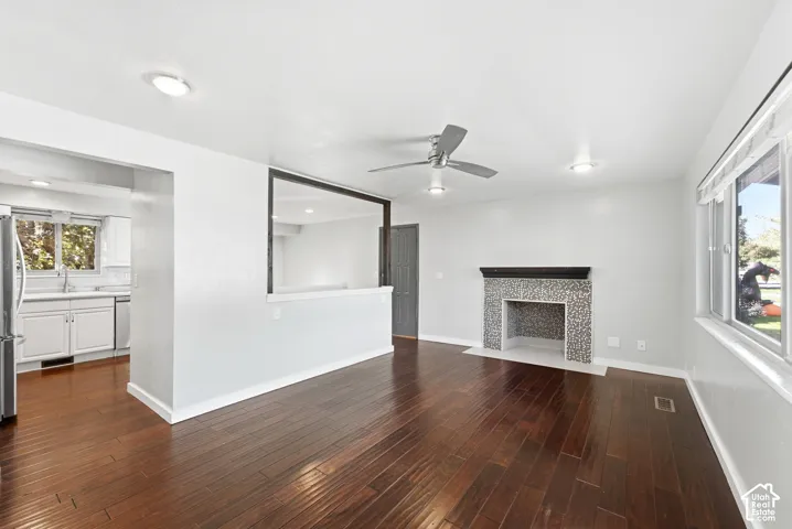 Rich wood-finish flooring, a tiled fireplace with dark mantel, and a modern ceiling fan with recessed lighting
