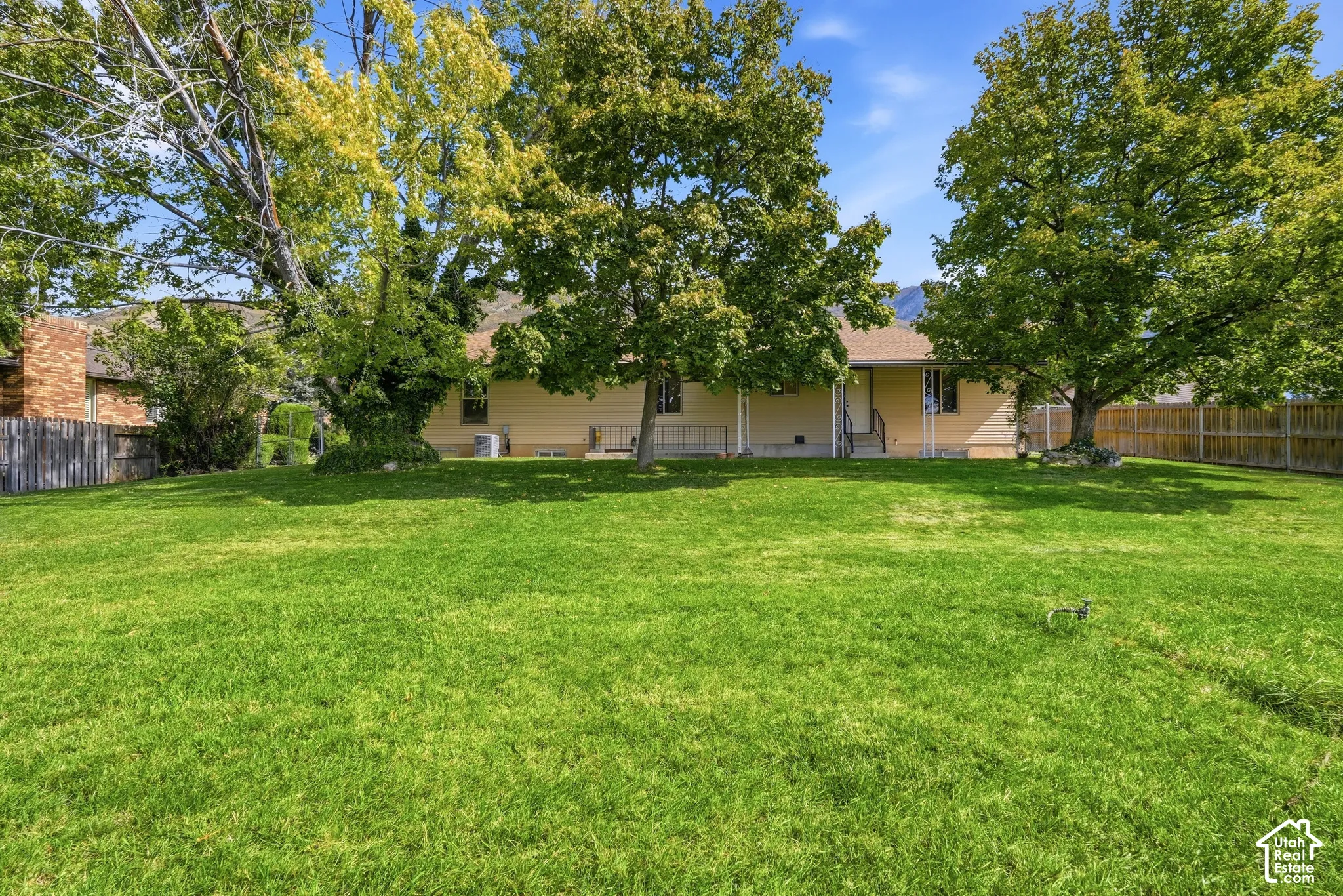 Expansive lawn with mature trees, a wooden privacy fence, and a brick chimney