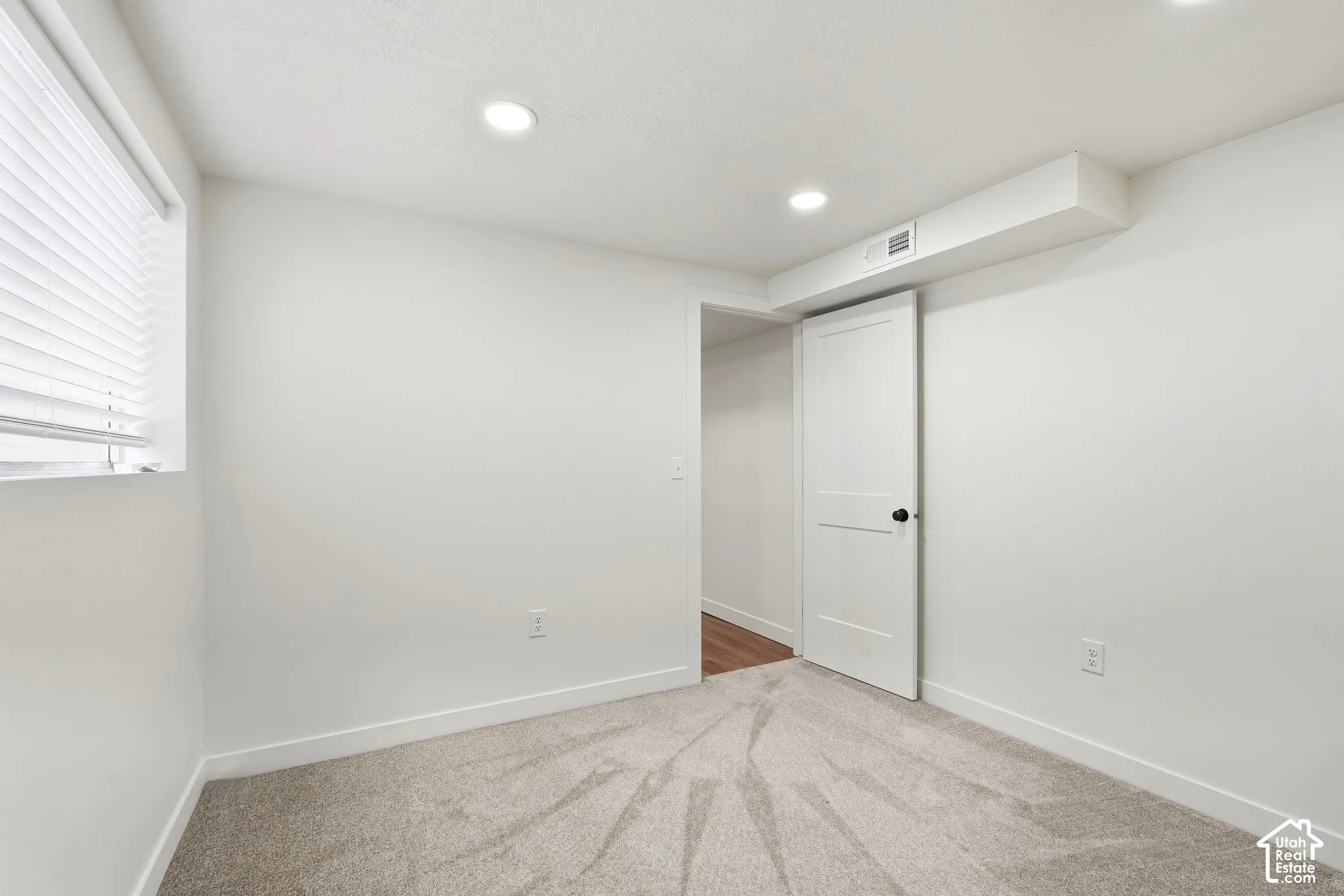Recessed lighting, light-colored walls, window with blinds, carpeted flooring, white interior door