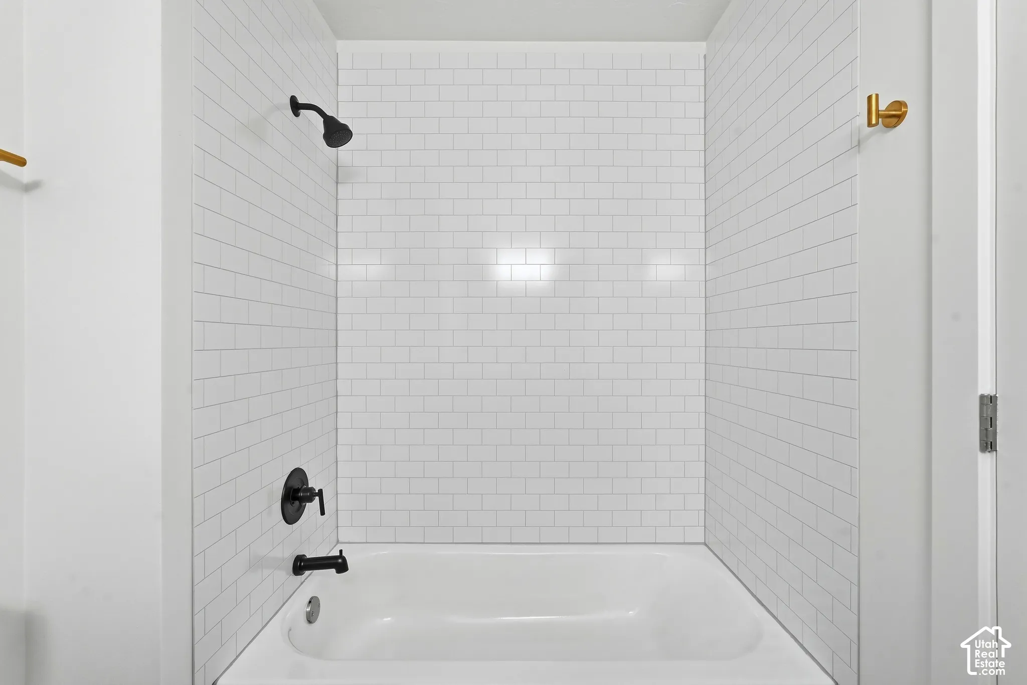 Bathtub with subway tile surround, matte black shower fixtures, and a wall-mounted towel bar