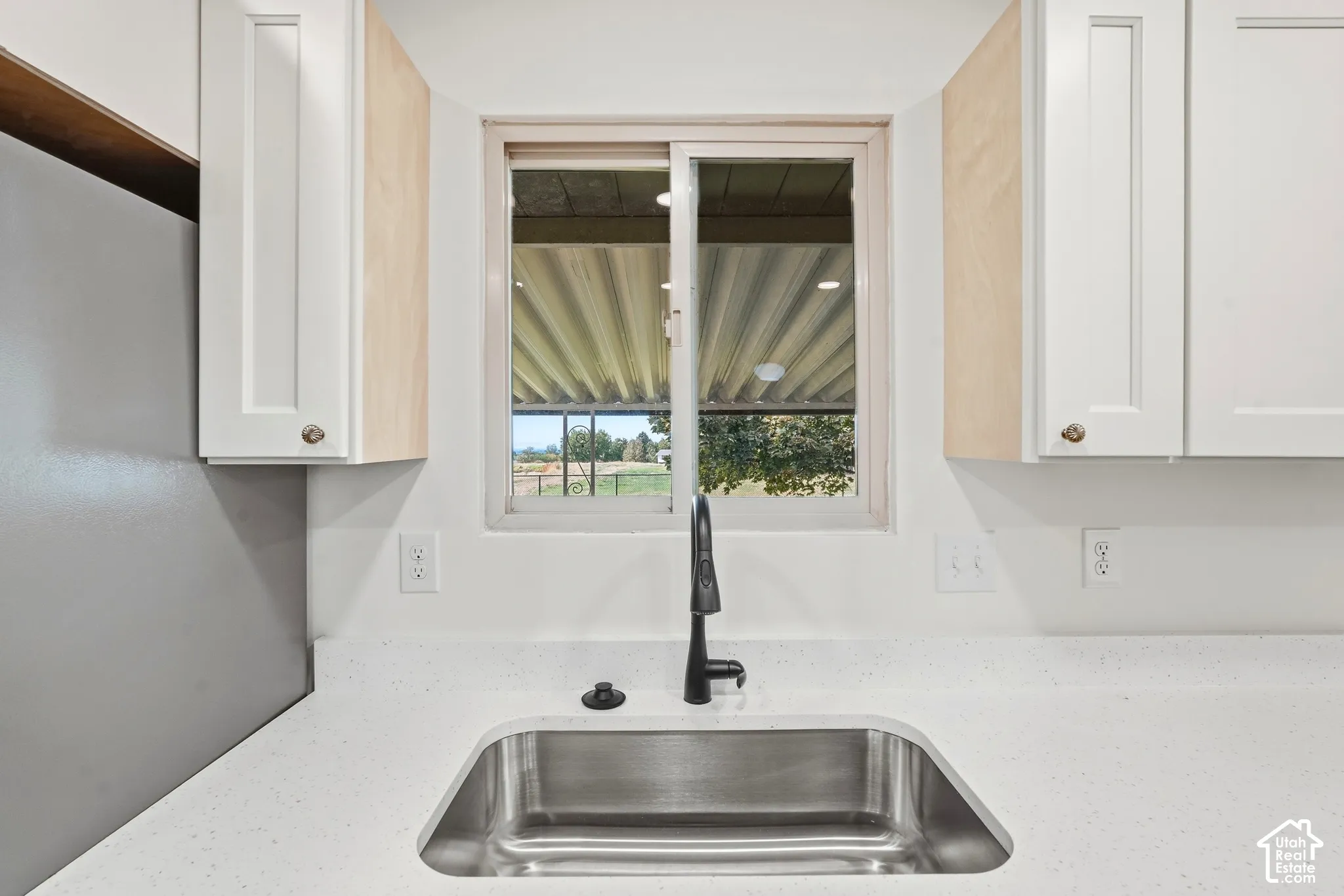 White shaker-style cabinetry, stainless steel undermount sink, matte black faucet, and light-toned solid surface countertops