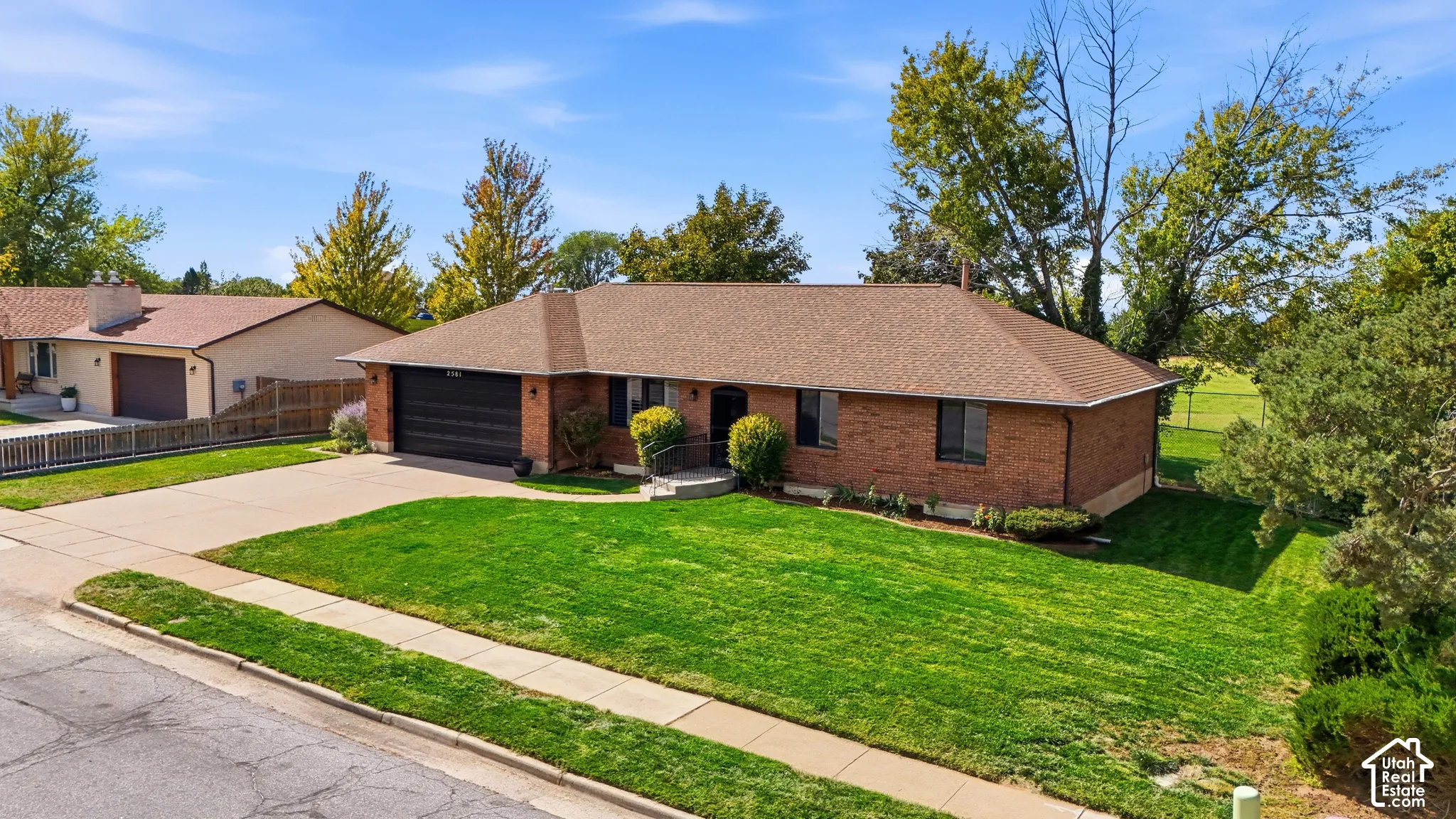 Brick exterior, attached two-car garage, concrete driveway, front yard with mature landscaping, and a brown shingle roof