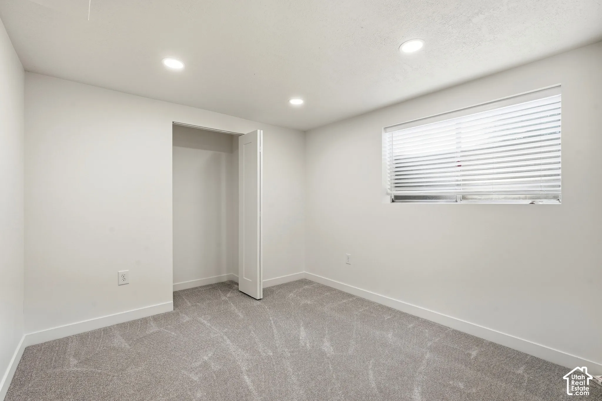 Recessed lighting, light gray plush carpeting, white walls, and a window with horizontal blinds