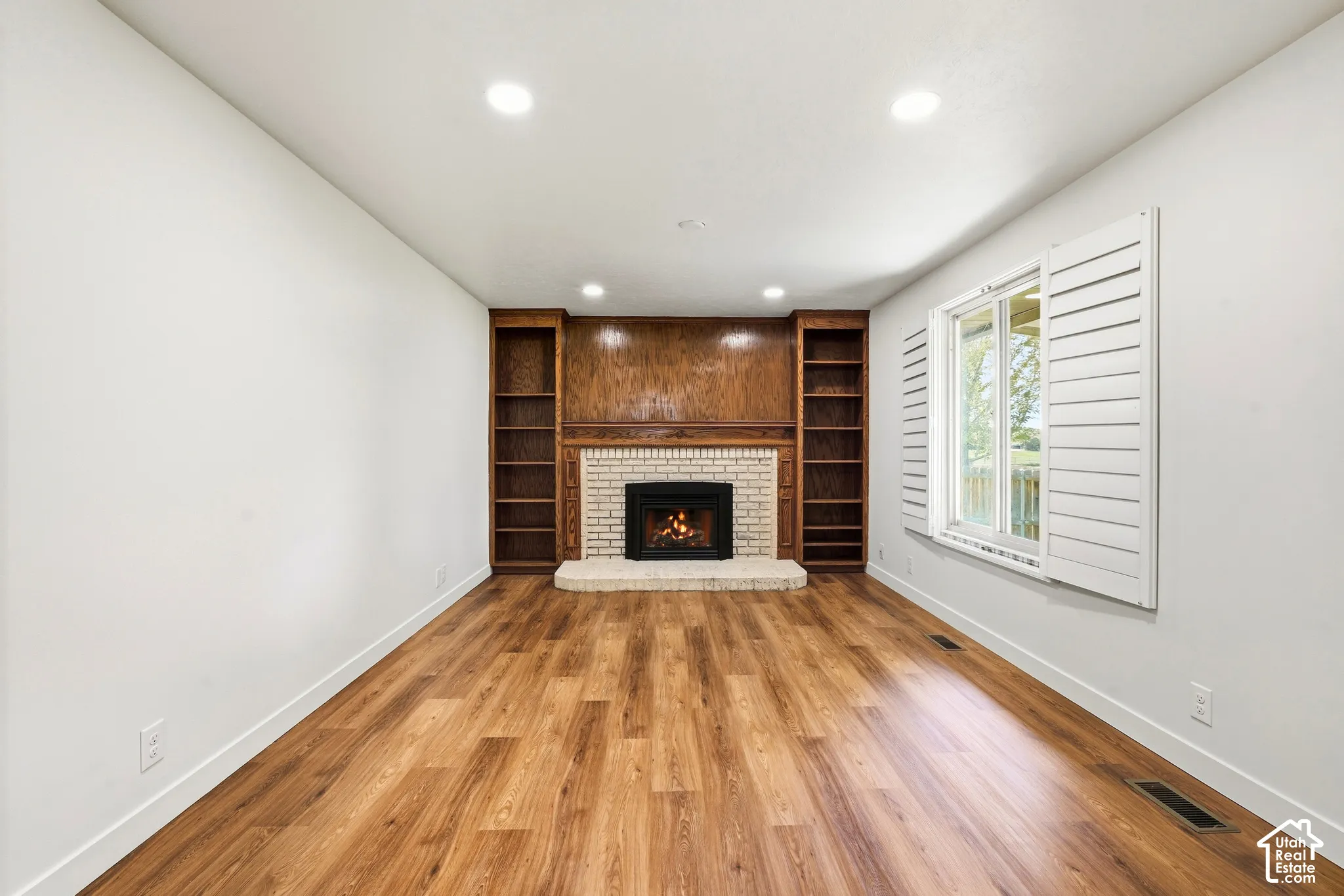 Living room off of Kitchen. Fireplace with a brick surround and hearth, flanked by built-in wood-finish shelving and cabinetry