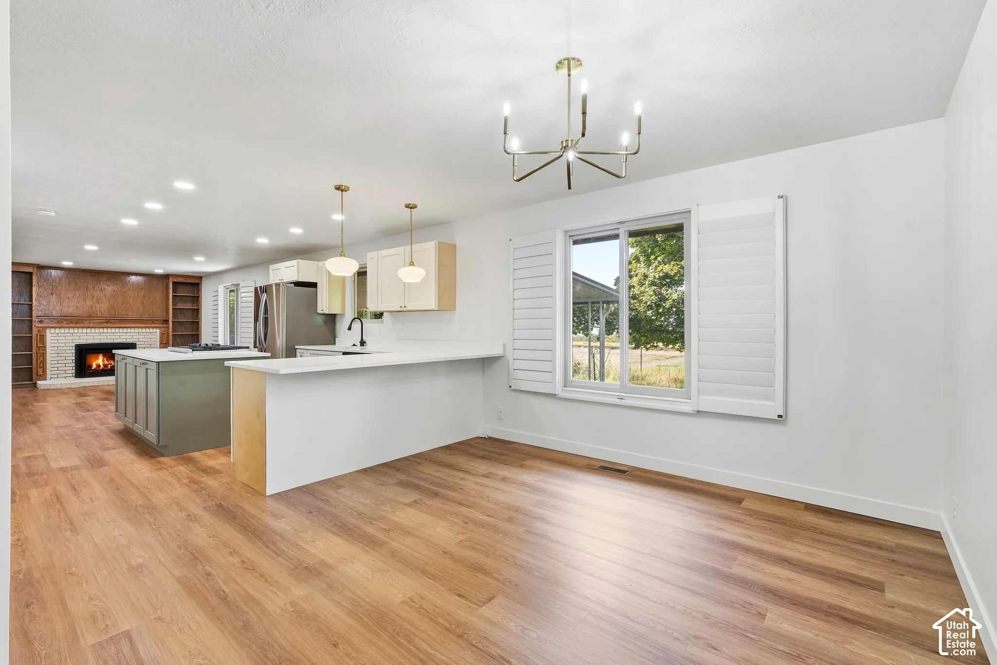 Open-concept interior featuring wood-finish flooring, a kitchen island with seating, a fireplace with a white brick surround, and built-in shelving