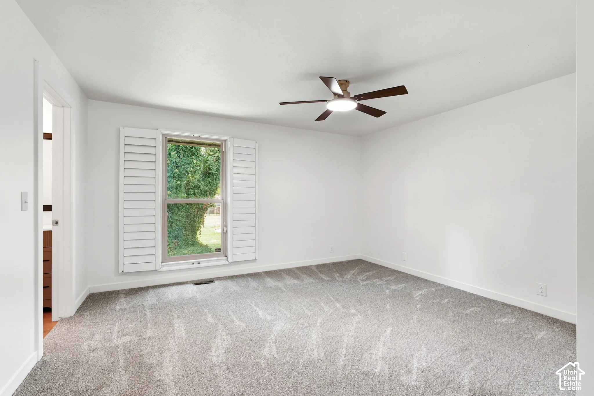 Primary Carpeted room with white walls, a ceiling fan with integrated lighting, and a window featuring white plantation shutters