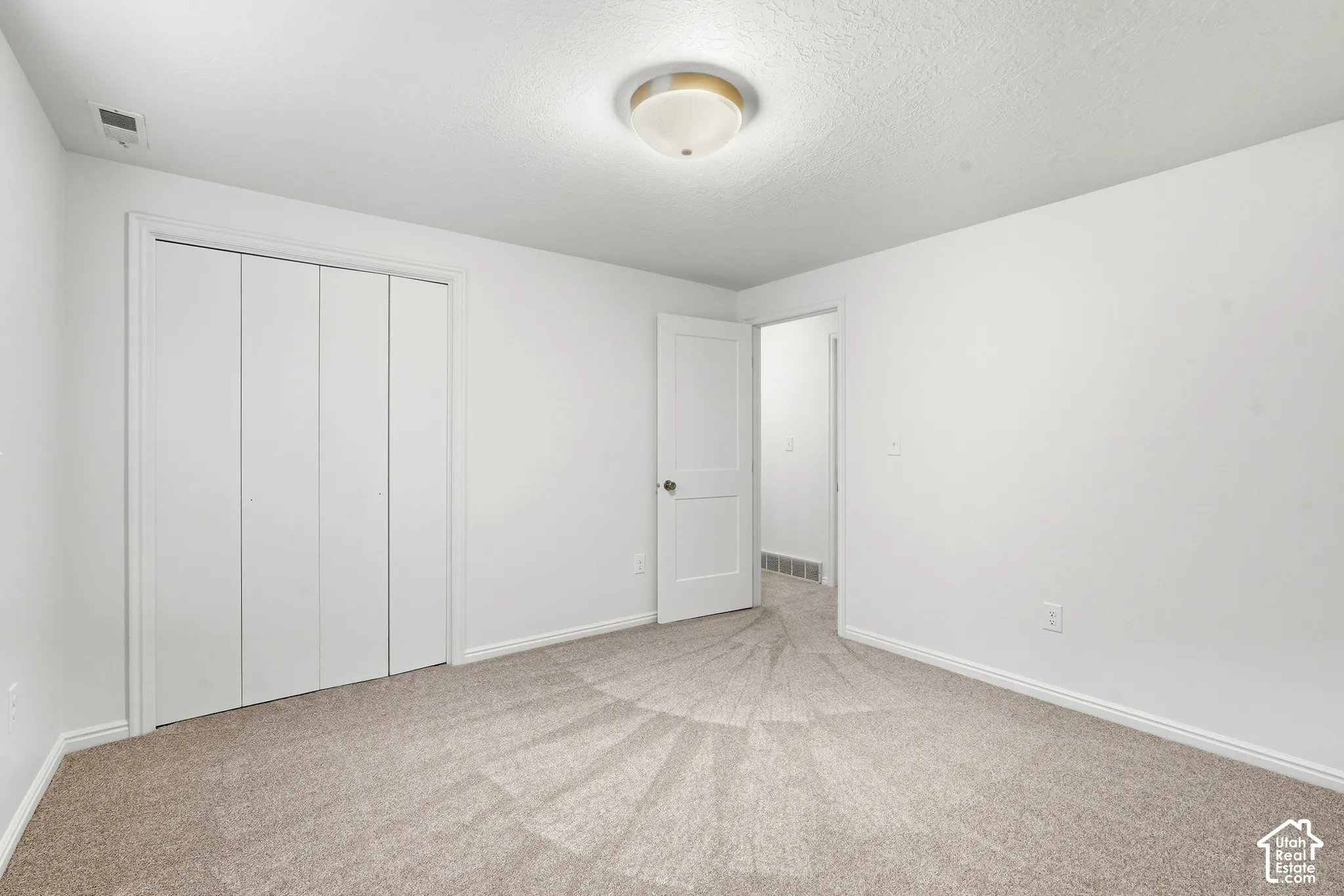 Wall-to-wall carpeting with a neutral tone, ceiling-mounted light fixture, and white bi-fold closet doors