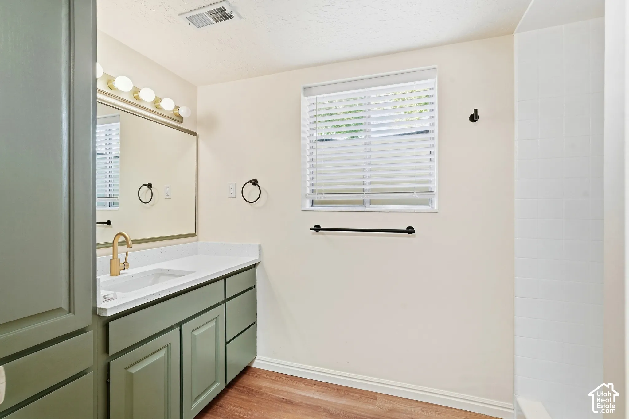 Green-finish vanity with an integrated sink and gold-tone faucet, complemented by a broad mirror with globe lighting