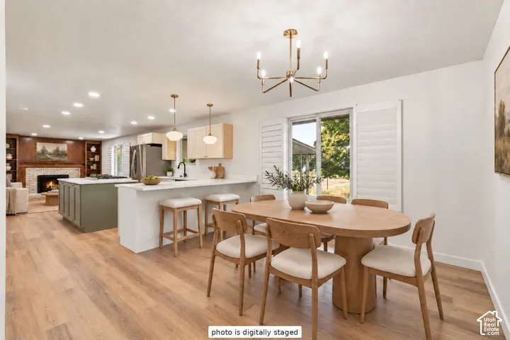 Open-concept kitchen and dining area featuring wood-finish flooring, a kitchen island with stone-finish countertops, recessed lighting, a multi-arm chandelier, and plantation shutters