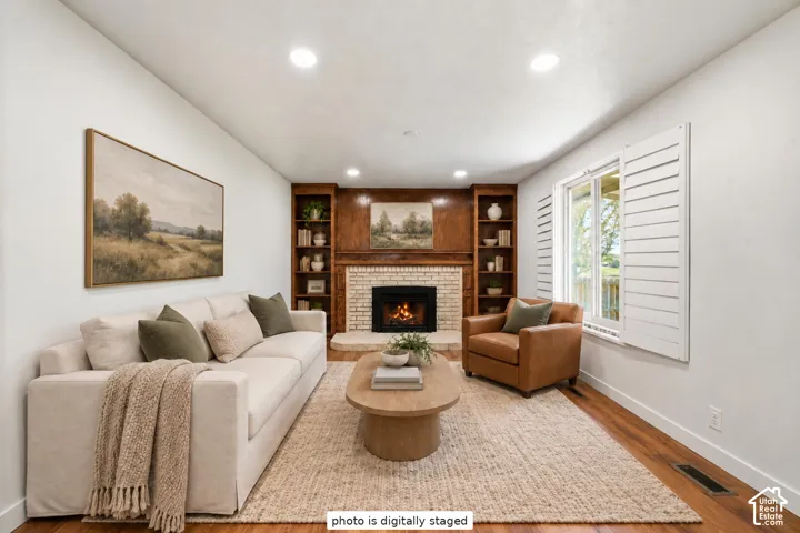 Living area featuring a floor-to-ceiling wood-panelled fireplace surround, built-in wooden shelving, light-toned brick hearth, recessed ceiling lighting, and plantation shutters