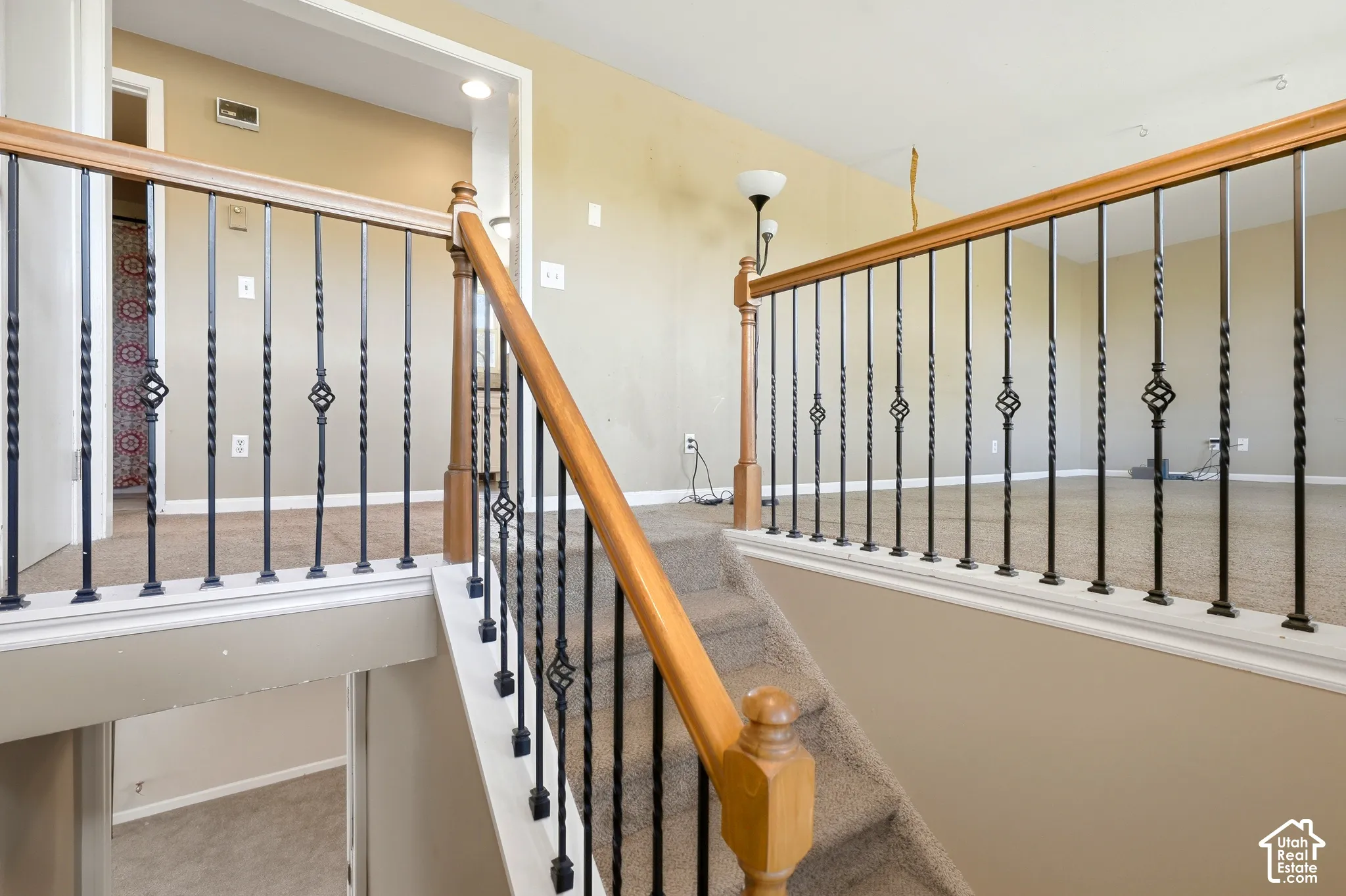 Carpeted staircase featuring wrought iron balusters and a wood-finish handrail