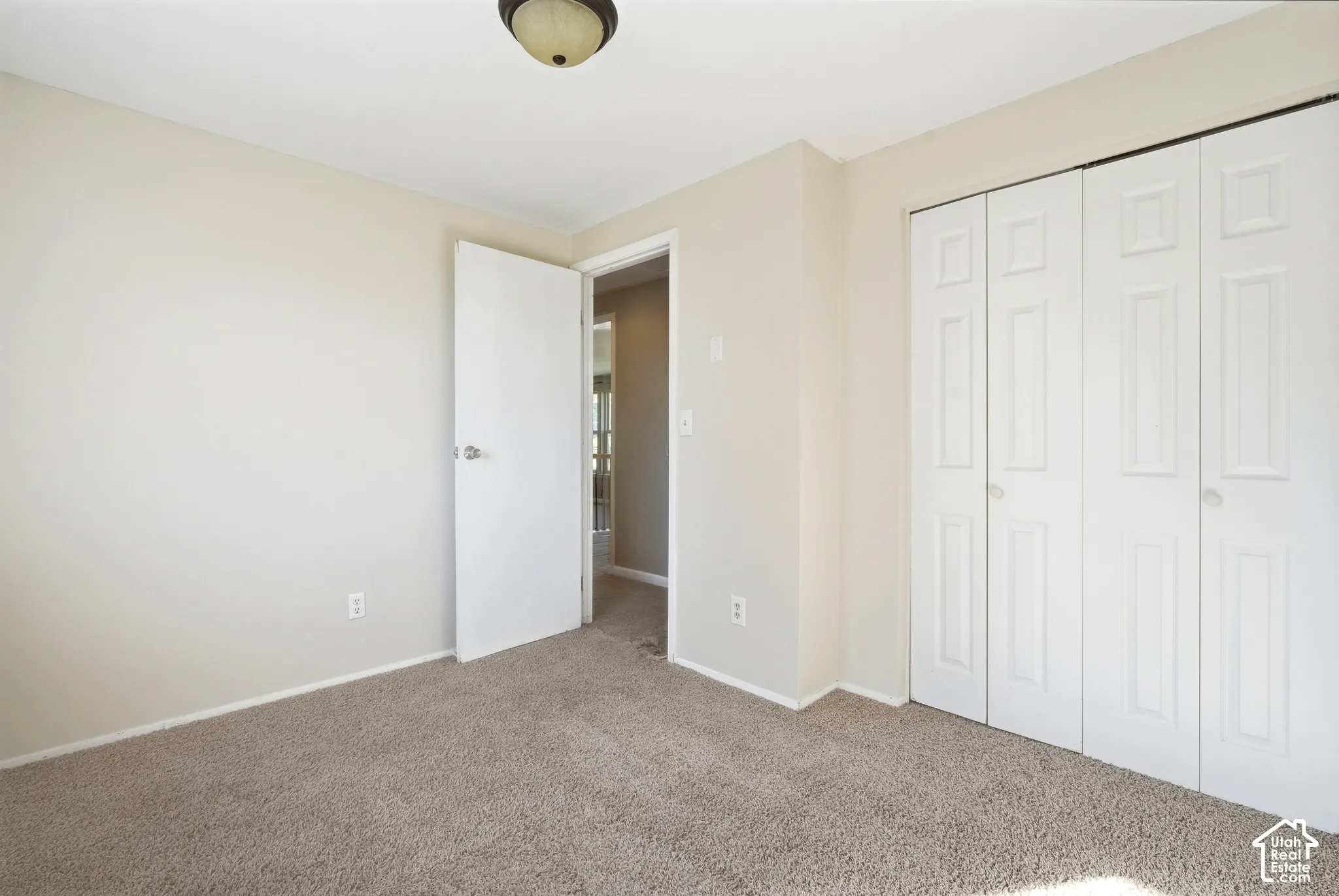 Neutral tone wall paint, carpet flooring, a ceiling-mounted light fixture, a white interior door, and bi-fold closet doors