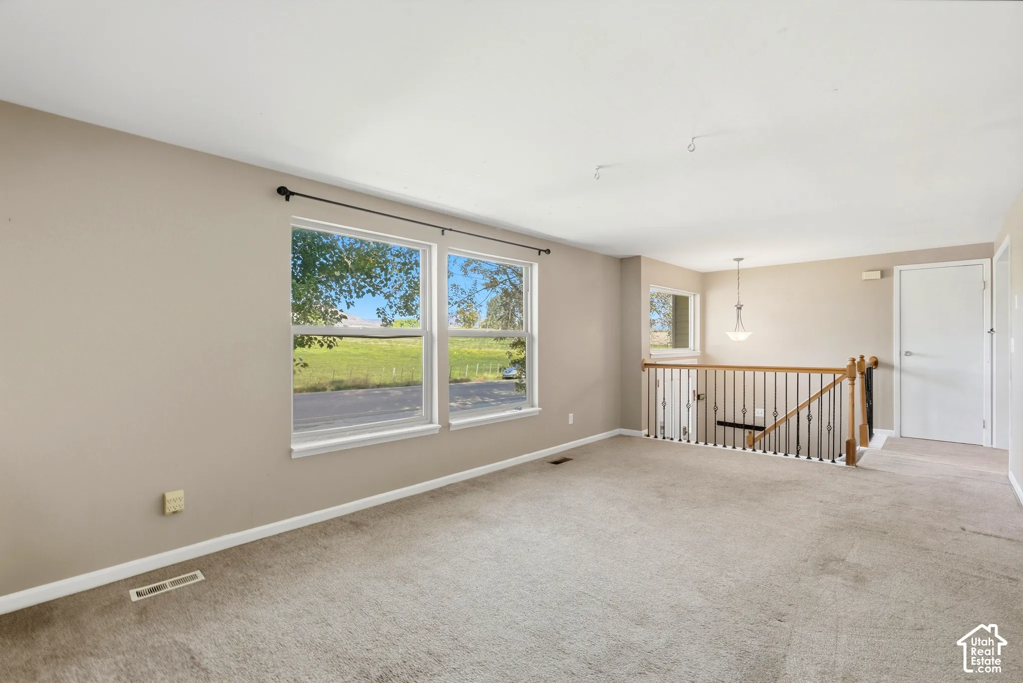 Neutral-toned wall paint, carpeted flooring, multiple windows, and a staircase with wood and metal railings