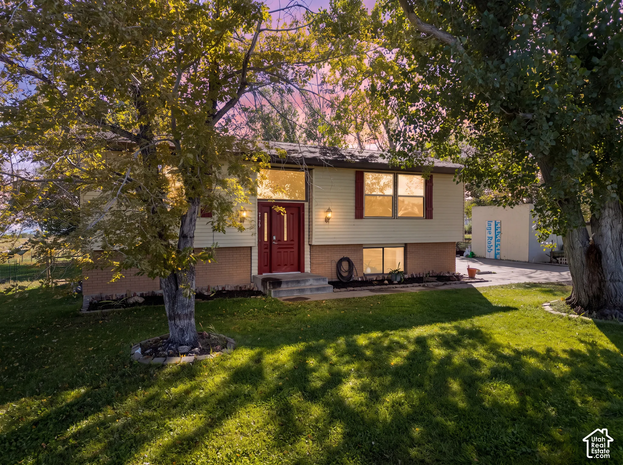 Split-level residence featuring a red entry door, brick foundation, and light-colored siding