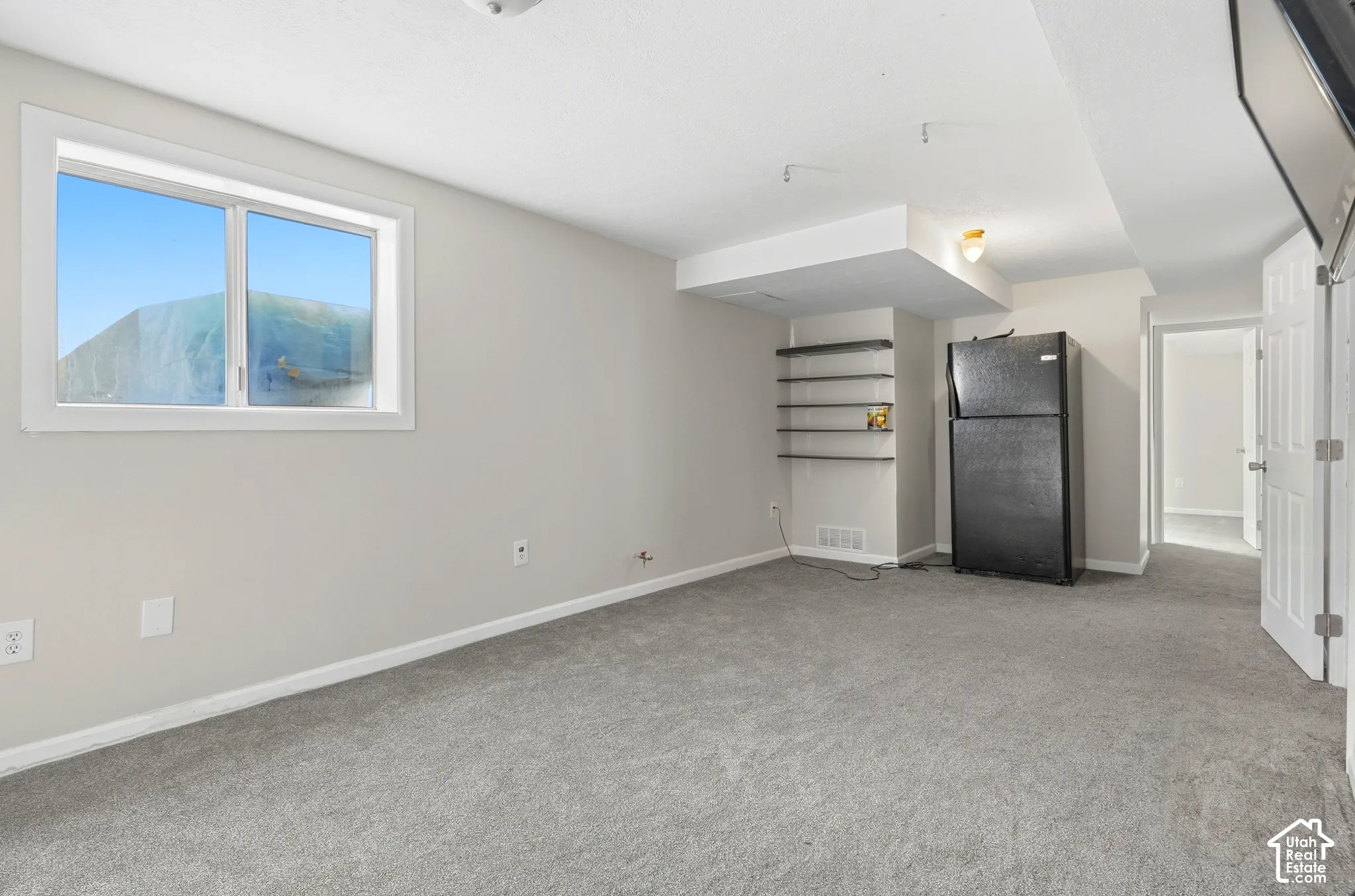 Recessed window with white trim, gray carpeting, built-in shelving, and a black refrigerator