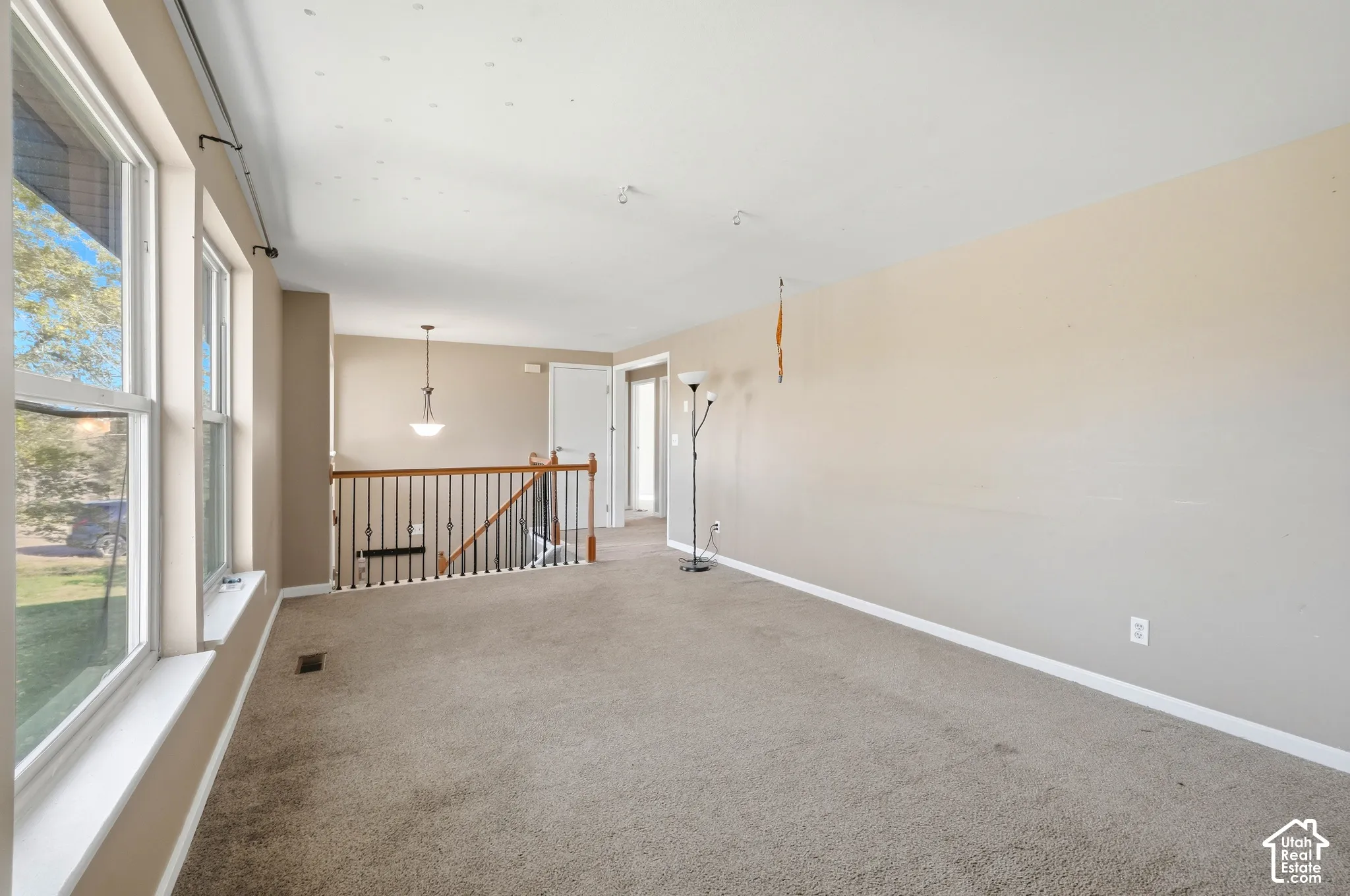 Carpeted living area with multiple windows, a ceiling-mounted light fixture, and a staircase featuring a wood handrail with metal spindles