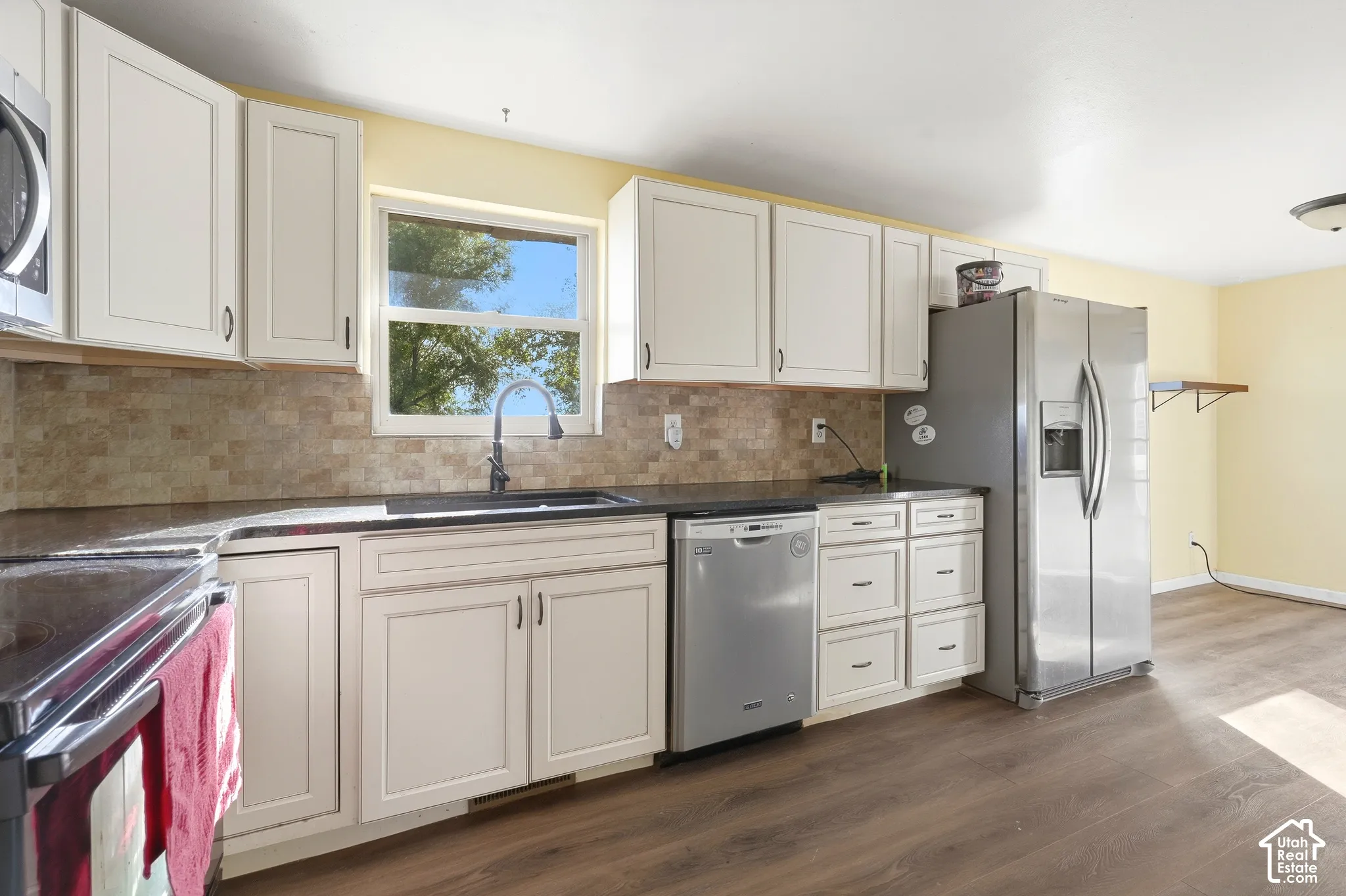 Kitchen featuring white cabinetry, dark countertops, a tile backsplash, and wood-finish flooring