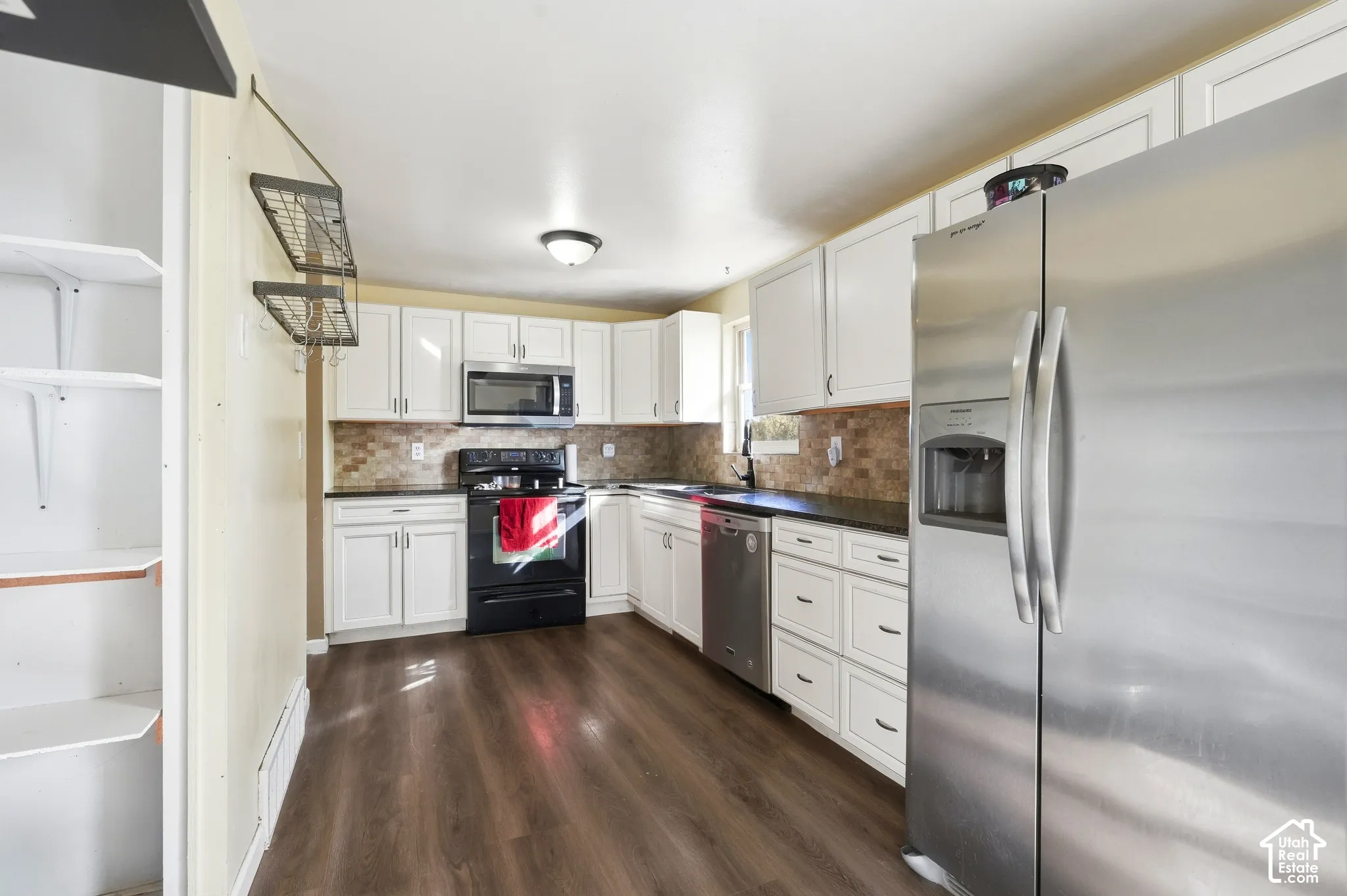 Kitchen featuring white cabinetry, dark countertops, a tiled backsplash, stainless steel appliances, and wood-finish flooring