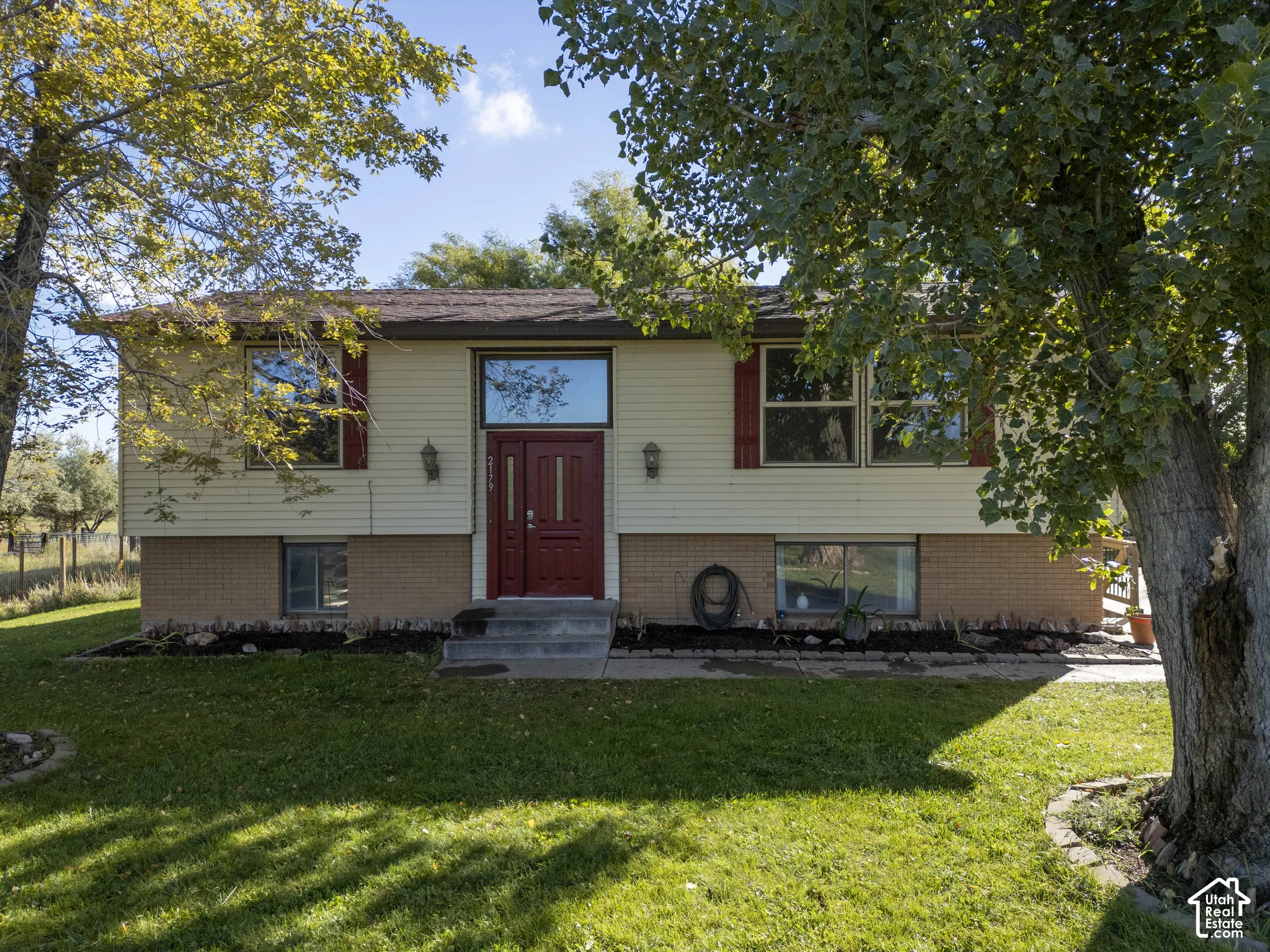 Split-level residence featuring light-colored siding, a prominent red double entry door, and contrasting red window shutters