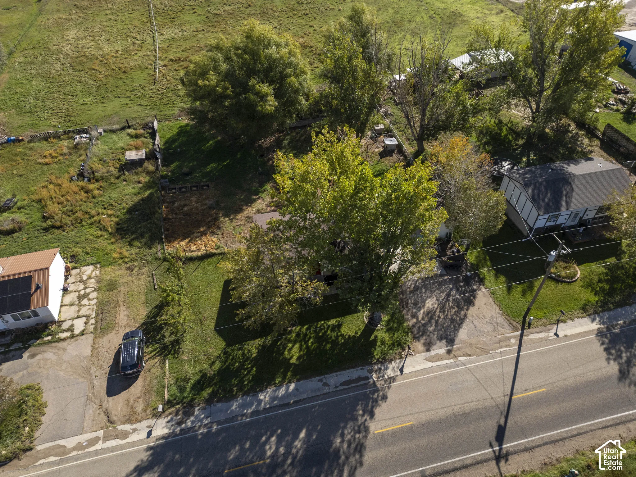 Expansive property with a paved road frontage, mature trees, and a detached structure with solar panels