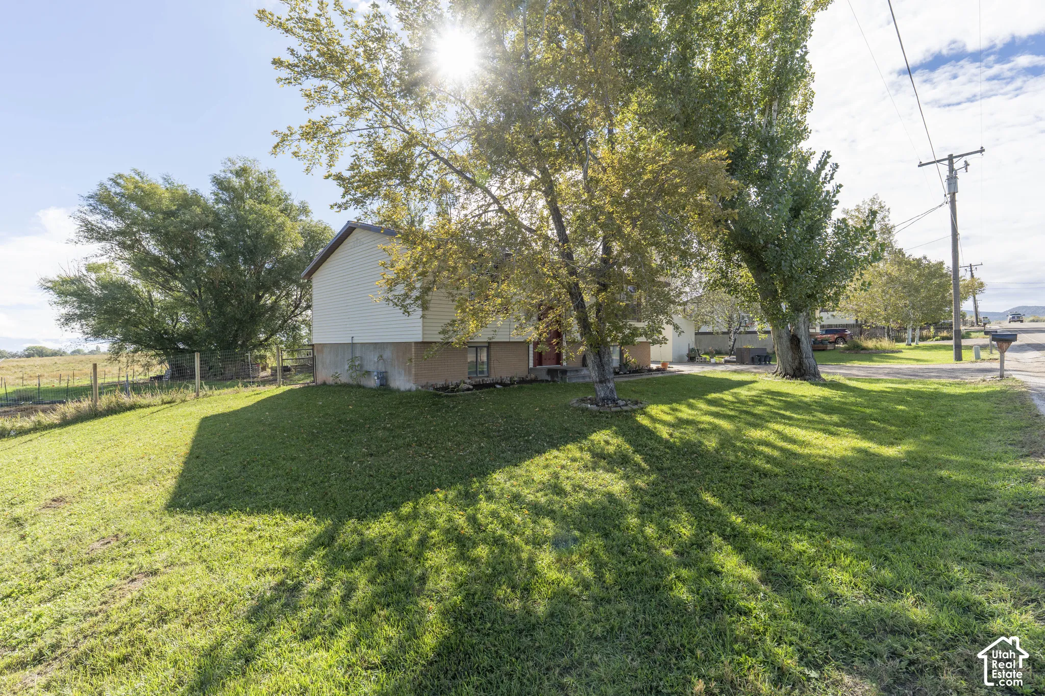 Expansive lawn area with mature trees and a two-story residence featuring light-colored siding
