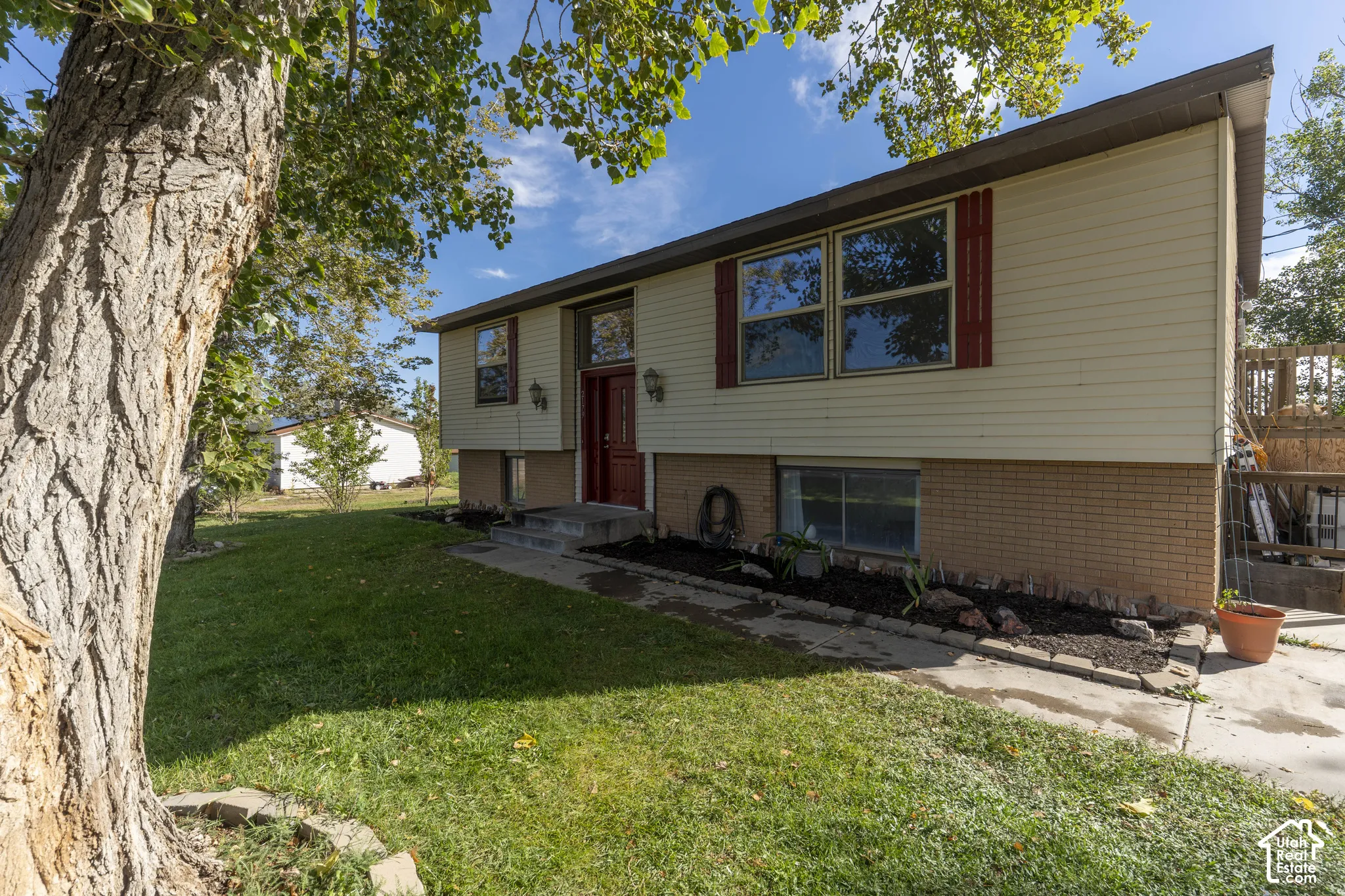 Split-level home featuring light-colored siding, red shutters, and a red entry door