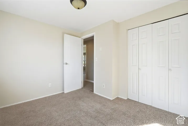 Neutral tone wall paint, carpet flooring, a ceiling-mounted light fixture, a white interior door, and bi-fold closet doors
