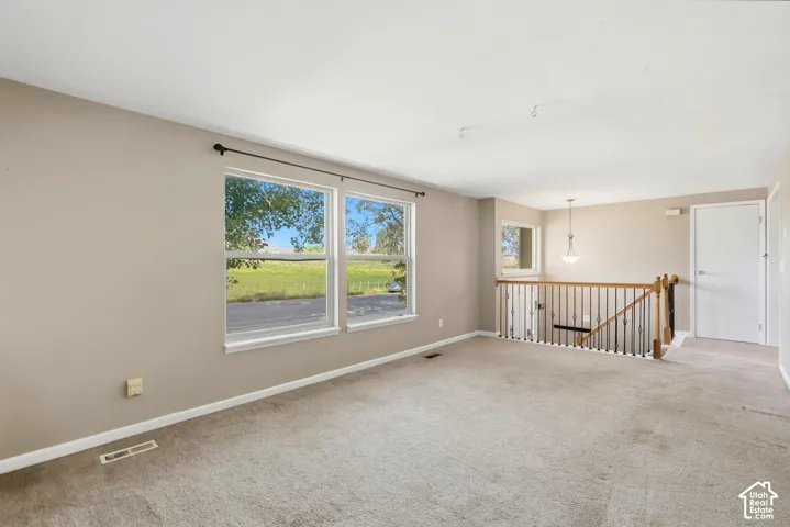 Neutral-toned wall paint, carpeted flooring, multiple windows, and a staircase with wood and metal railings