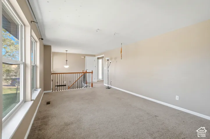 Carpeted living area with multiple windows, a ceiling-mounted light fixture, and a staircase featuring a wood handrail with metal spindles